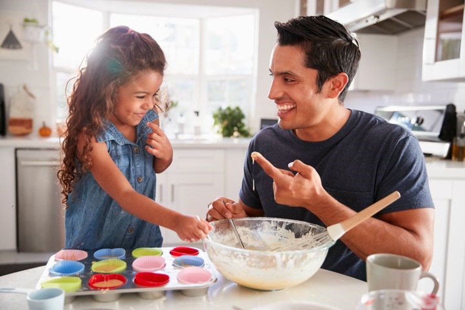 A smiling adult and child baking cupcakes in a kitchen