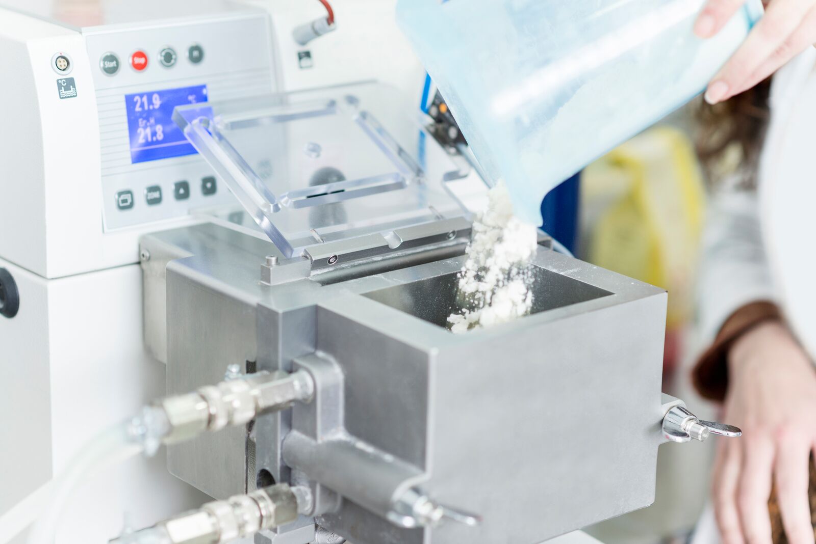 Flour being poured into equipment by a woman's hand with a blue measuring cup
